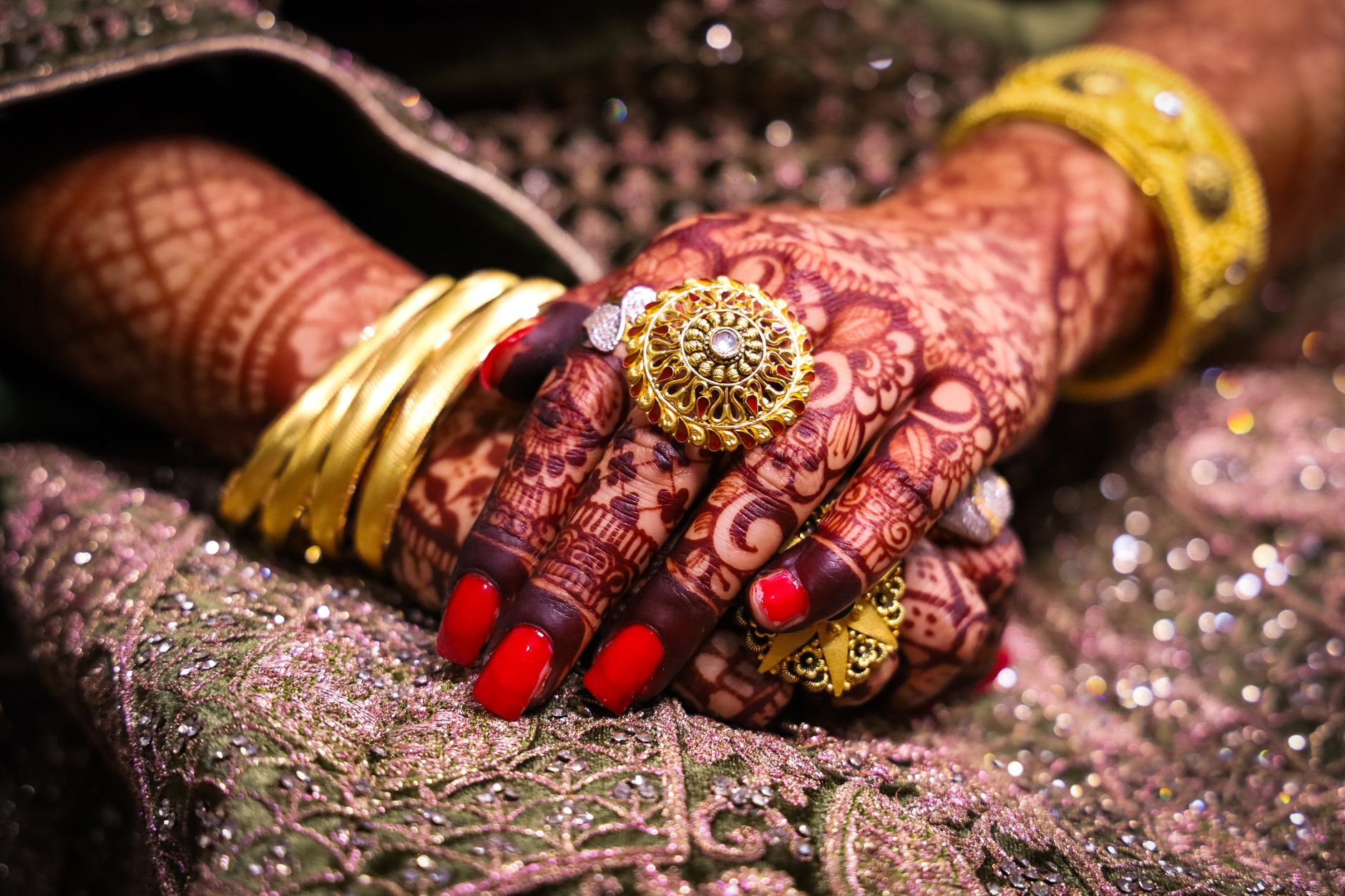 Close-up of beautifully hennaed hands adorned with traditional gold jewelry and vibrant fabrics. — About Truth Jewellery and