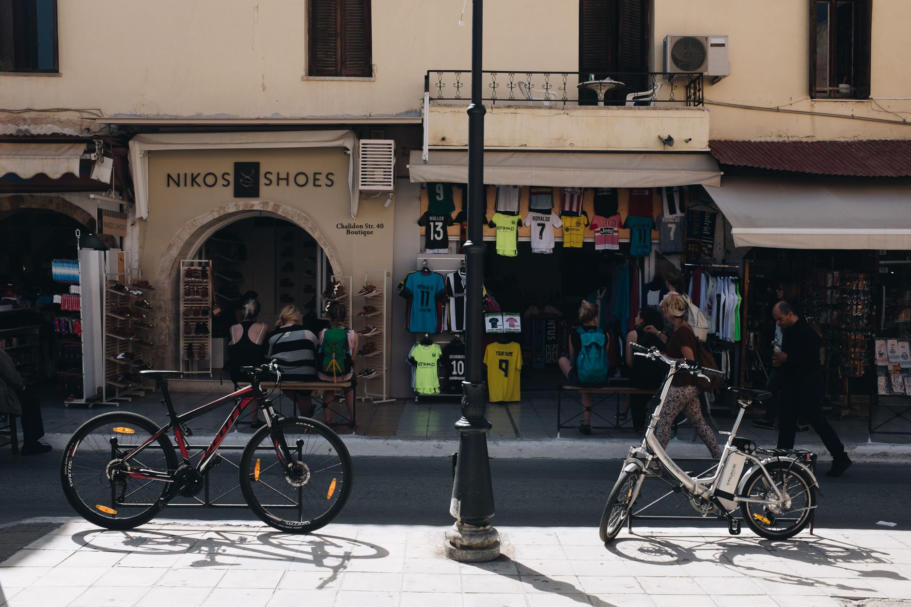 Bicycles parked on a street in Chania, Greece, in front of vibrant stores. — Celebrity Trends - Over The Knee Boots