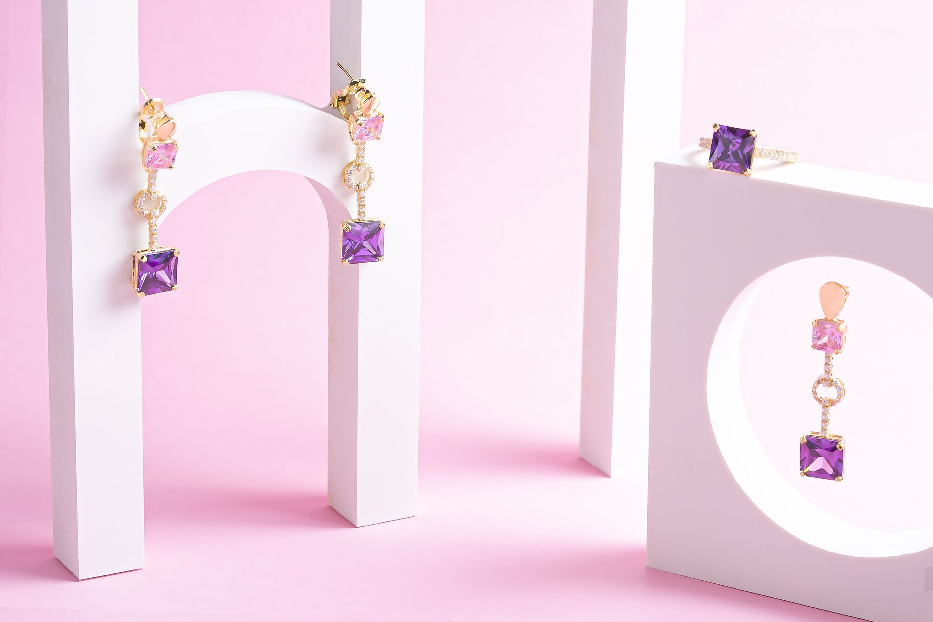 Minimalist display of gold jewelry with purple gemstones on a pink background. — Christening Jewellery - The Best Option of G