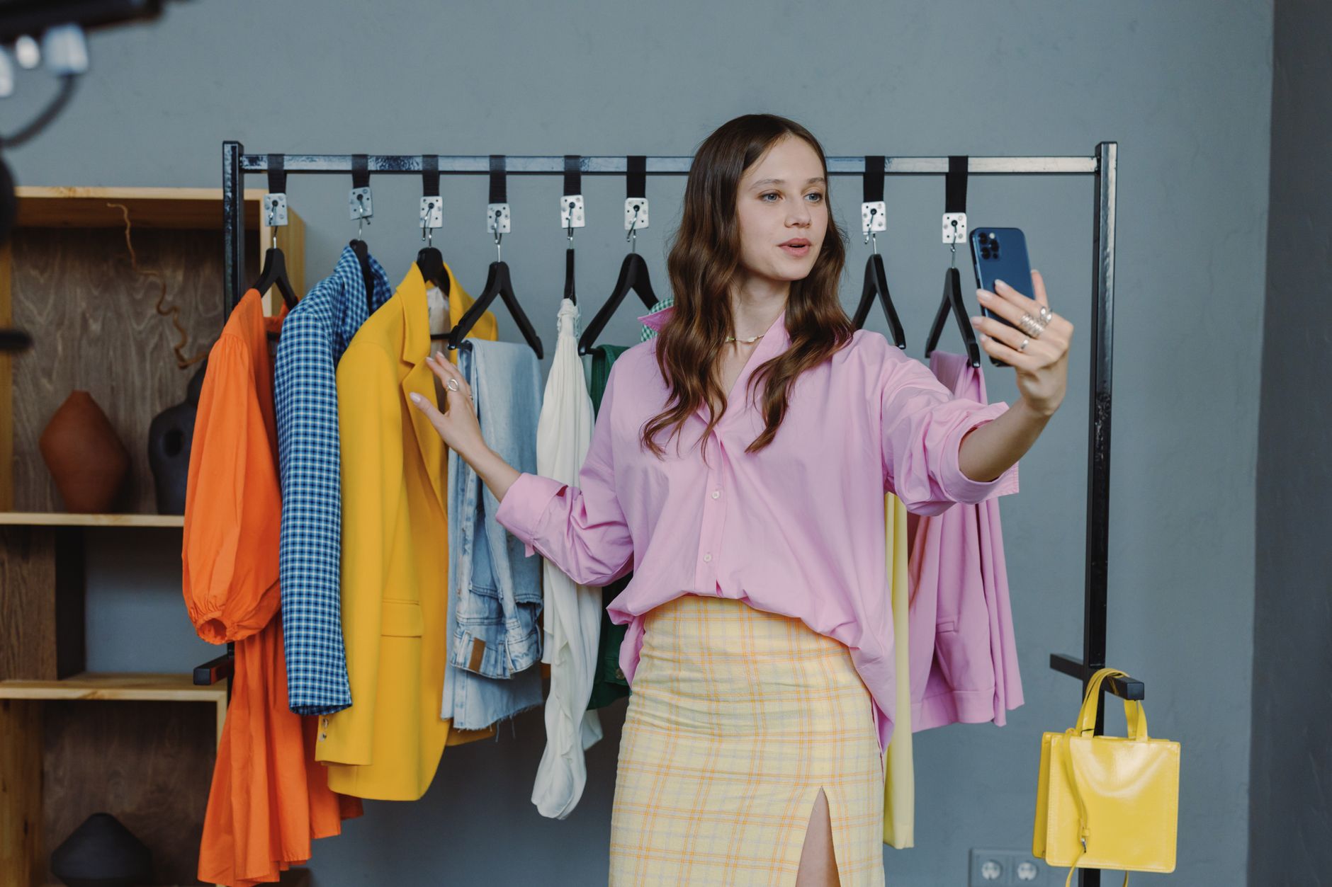 A young woman taking a selfie in front of a colorful clothes rack indoors. — Fred Perry Clothing - A Brief History and Inform