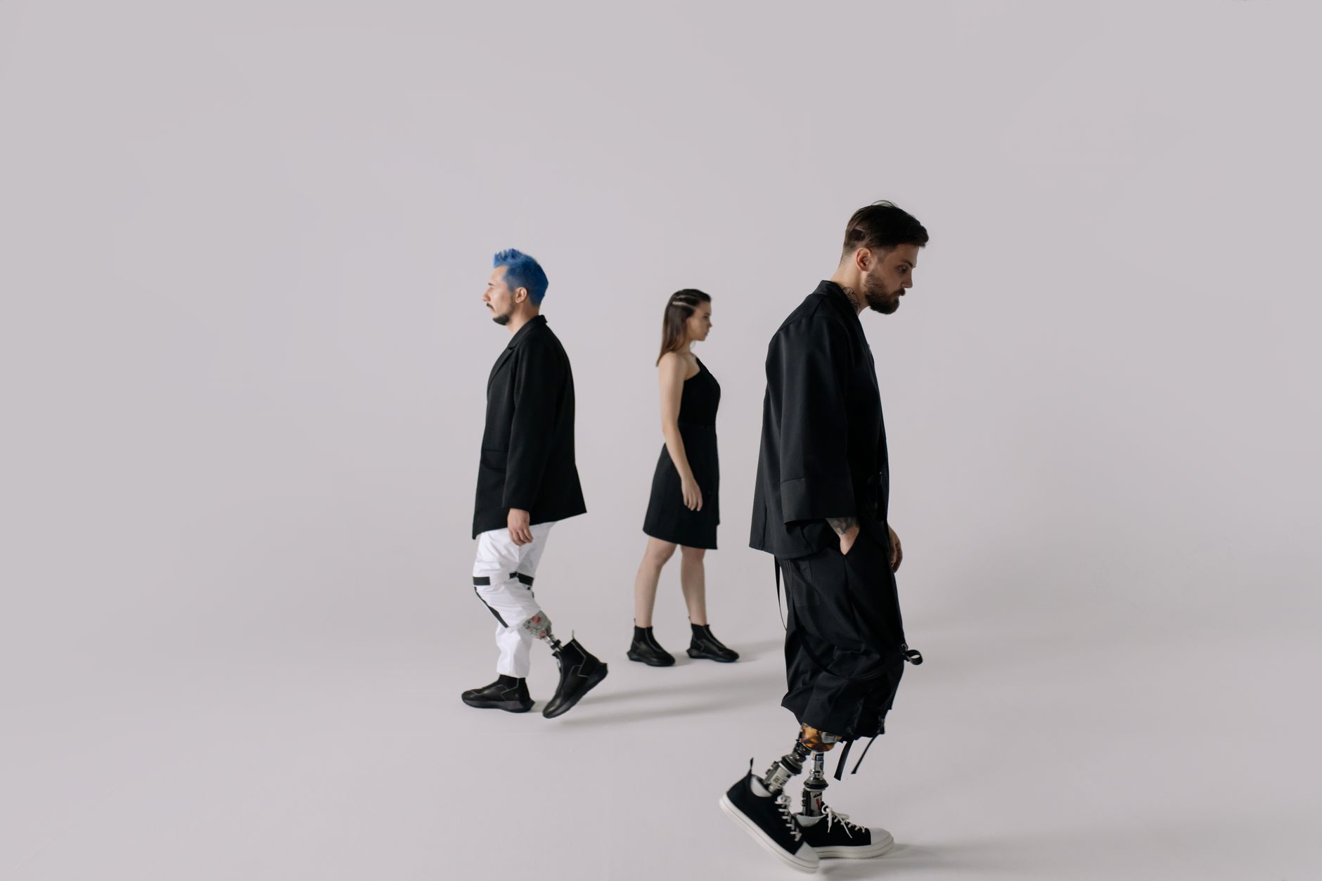 Three adults walking indoors; one wearing prosthetic legs, others in modern attire. — Haircut for Men with Long Hair