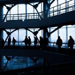 Silhouettes of people walking in a modern architectural building with large windows. — How MetaTrader 4 for macOS Combines Po