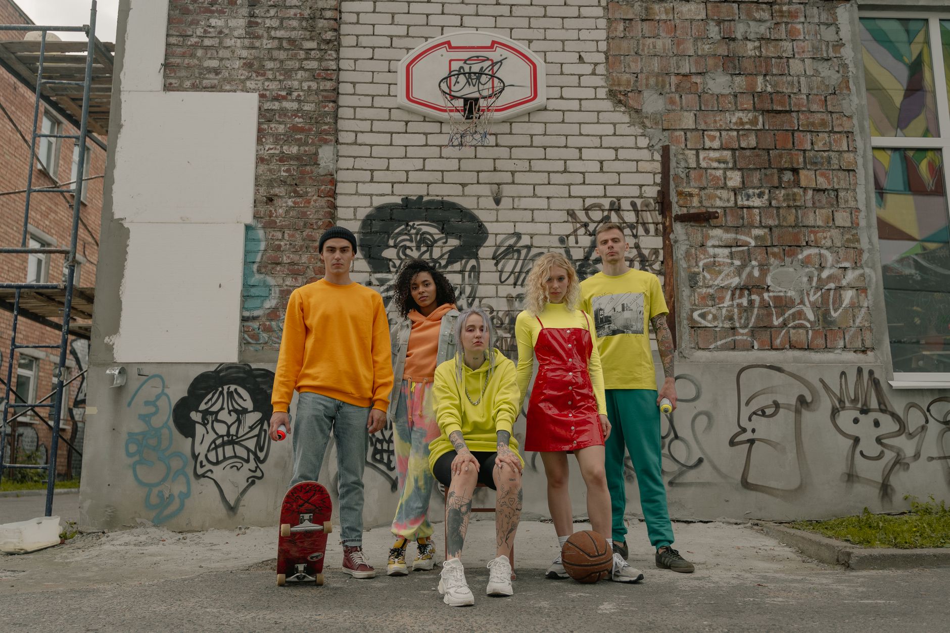 A diverse group of young adults posing in front of a graffiti-covered wall and basketball hoop. — How to Dress Like a Celebri