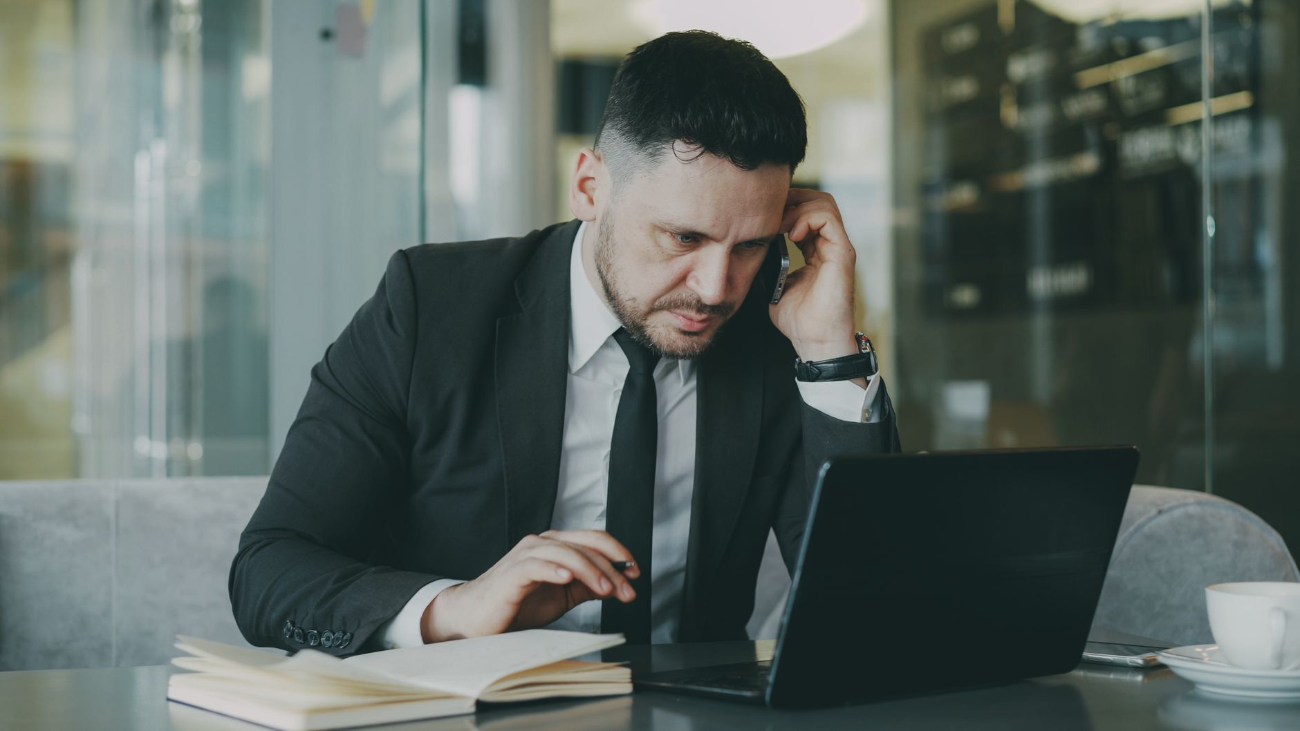 Focused businessman in suit multitasking on phone and laptop in modern office. — How to Get a Free Background Check in Virgin