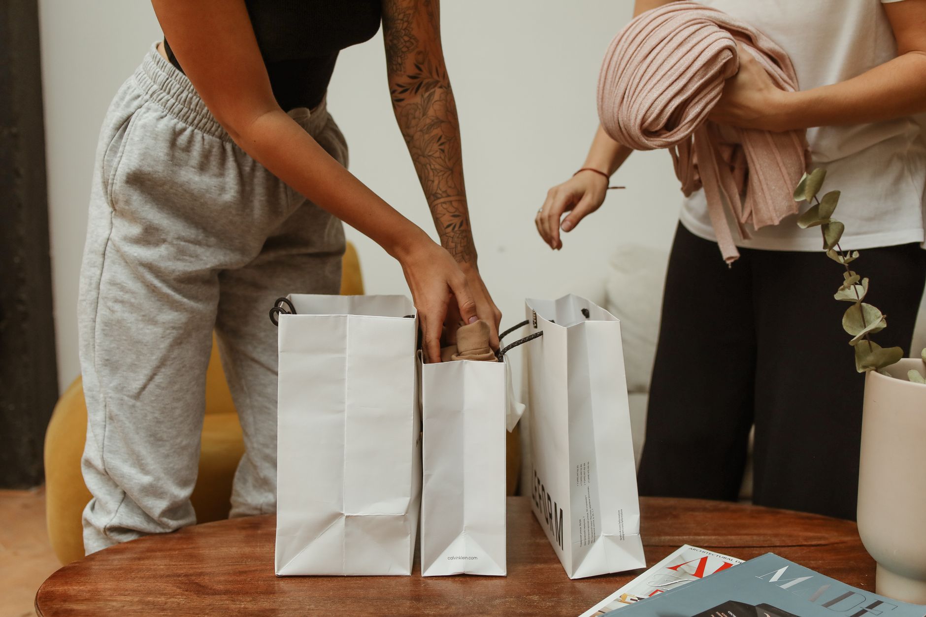 Two young adults unpacking shopping bags with clothing in a cozy indoor setting. — Presenting Necklaces from 6th Street to Yo